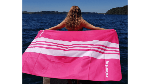 Pink Swimdry Sea Breeze Plus towel held beside the water