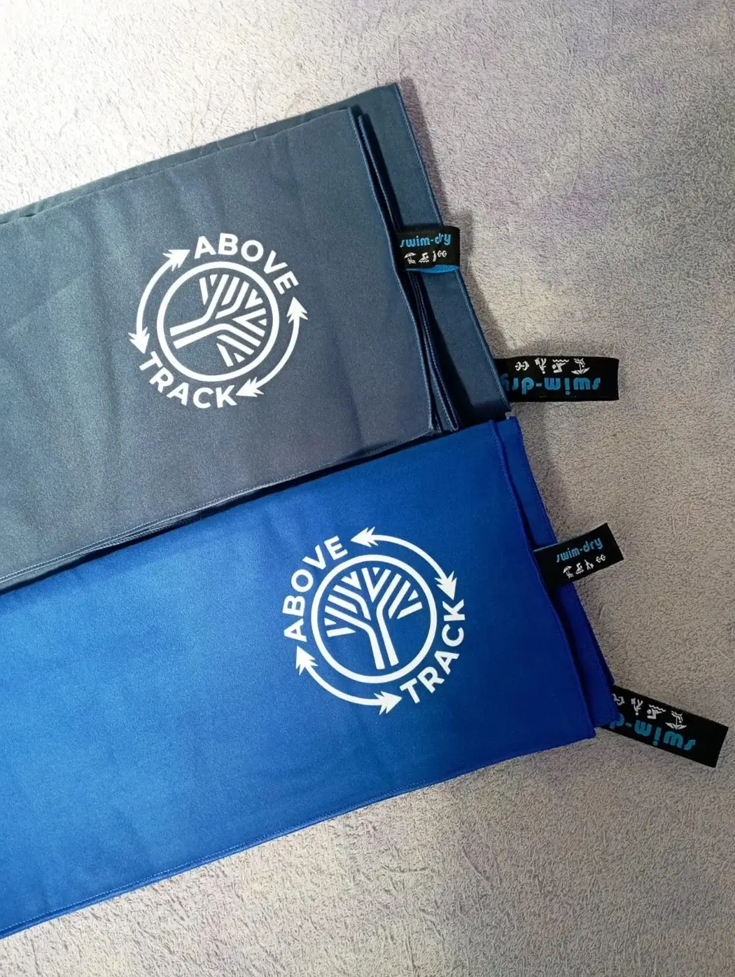 Grey and blue Swimdry towels displaying a custom white logo